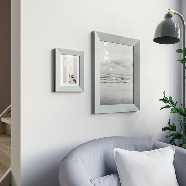 Kaks raami valgel seinal: üks taim, üks rand. Hall tugitool, taim, lamp all.