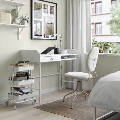 Kodukontori seadistus: valge RÅSKOG käru laua all koos esemetega, sülearvuti ja tarvikud laual, valge metalljalgadega tool.