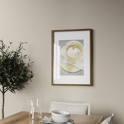 Kohvitass ripub seinal valge tooliga puidust laua kohal. Taim ja karahvin on laual. Raam mahutab pildi mõõtmetega kuni 50x70 cm.