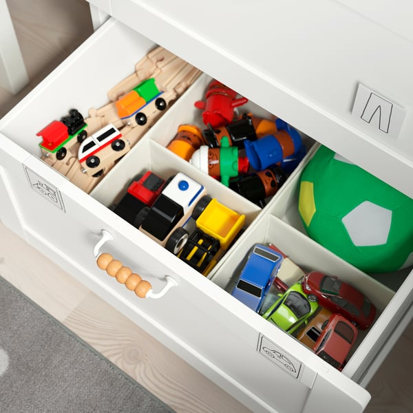 Valge mänguasjakirst jagatud sahtlitega, kus on erinevad värvilised mänguasjad.