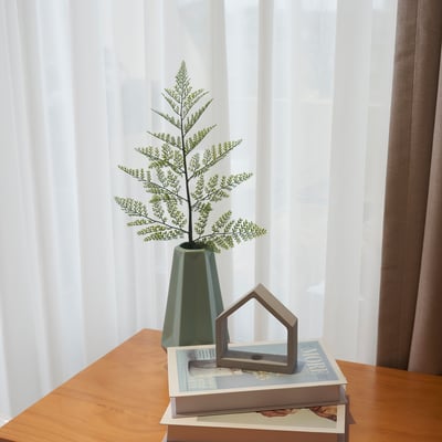 Roheline vaas taimega raamatutel akna lähedal.