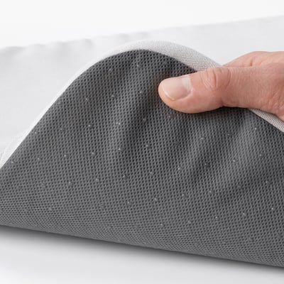 Käsi hoiab halli tekstuuriga toolipatja, mis näitab selle pehmet vahttäidist ja tõmblukku hõlpsaks pesemiseks.