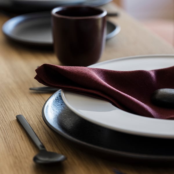 Elegantne lauakatmine tumeda linase salvrätiku, valge taldriku ja mustade söögiriistadega puidust laual, mis peegeldab esmaklassilist kvaliteeti ja stiilset disaini.