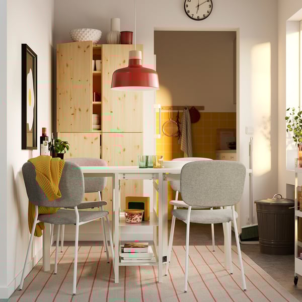 Väike söögikomplekt valge metalllaua ja hallide toolidega, puidust kapp, punane lamp.