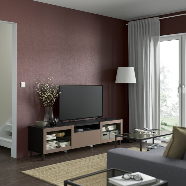A modern living room with a flat-screen tv on a light wood BESTÅ bench, grey couch, and large window with curtains.