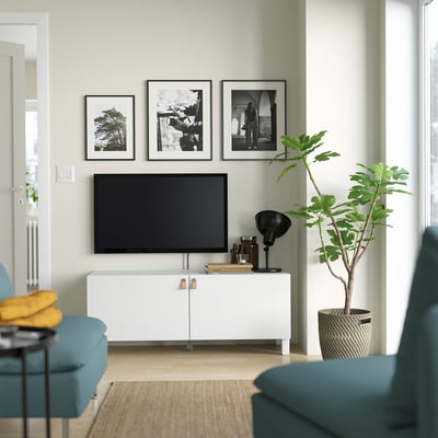 Modern living room with white BESTÅ tv unit, flat screen tv, framed photos, blue chair, and large plant.