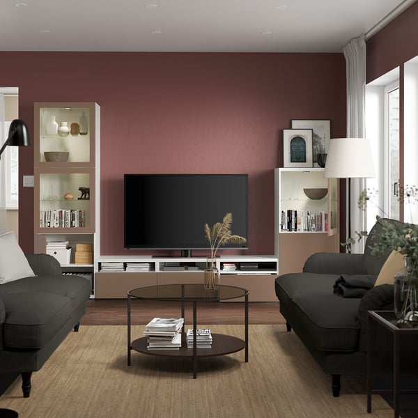 Modern living room with dark couches, wood floor, burgundy walls, tv, glass table, plants, decor.