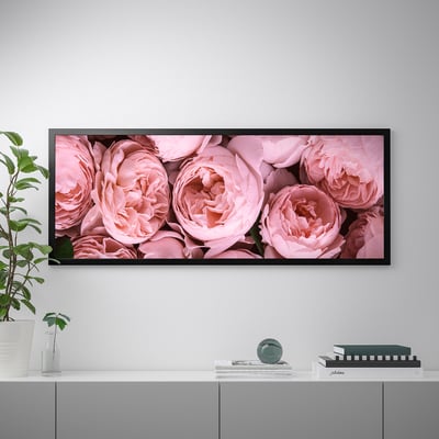 A framed canvas print of pink roses hangs on a wall above a cabinet with decorative items, including a vase with plant and stacked books.