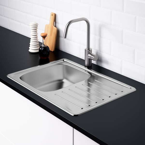 Stainless steel sink with drainer, installed in dark countertop, with items and tap.
