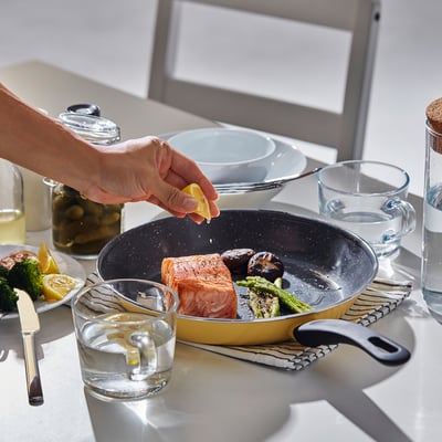 Hand squeezing lemon on salmon in HEMLAGAD frying pan on kitchen counter.