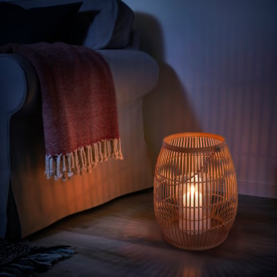 Wicker bamboo lantern, warmly lit, beside grey armchair with blanket.