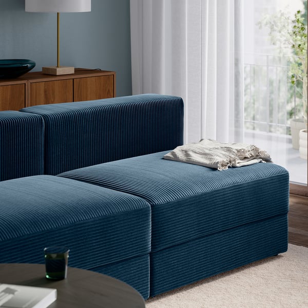 Dark blue sectional sofa with chaise, soft cushions, and hidden storage, positioned near a window.