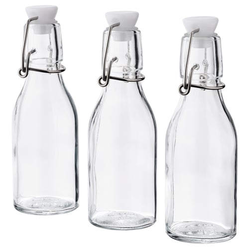 Three clear KORKEN glass bottles with white stoppers and metal clamps, arranged side by side.