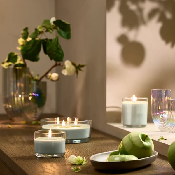 Lotsfägel scented candle, light blue, glass, round, on wooden table with fruit.