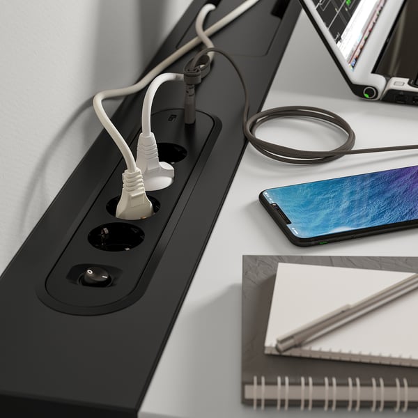 Black desk with built-in power sockets and usb ports, showcasing a smartphone, coiled charging cable, and notebook.