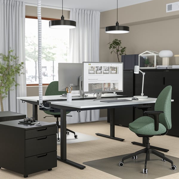 Modern home office with MITTZON desk, black, metal, rectangular, minimalist, large, with green chairs, computer, plants, and black cabinet.
