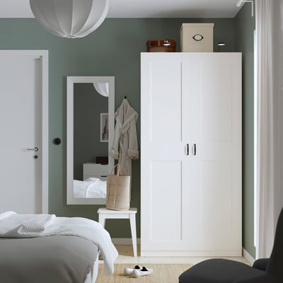 Modern bedroom with tall white PAX wardrobe, black handles, decorative boxes, mirror, wicker basket, and hanging lamp.