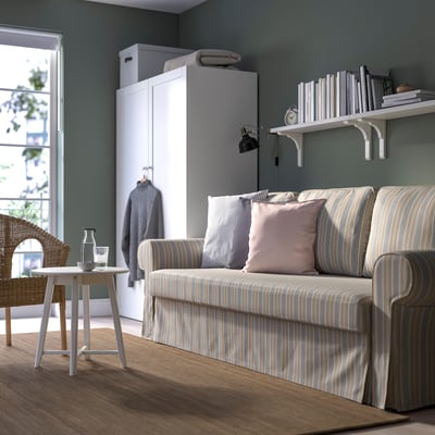 Modern living room with beige-grey striped sofa-bed, pink pillows, white coffee table, and grey sweater cabinet. Green walls, natural light.