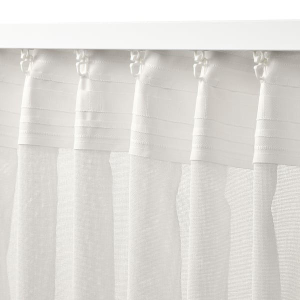 Cortines blanques transparents penjants, amb ganxos i llum filtrant-se. Ideal per a finestres amples o looks en capes.