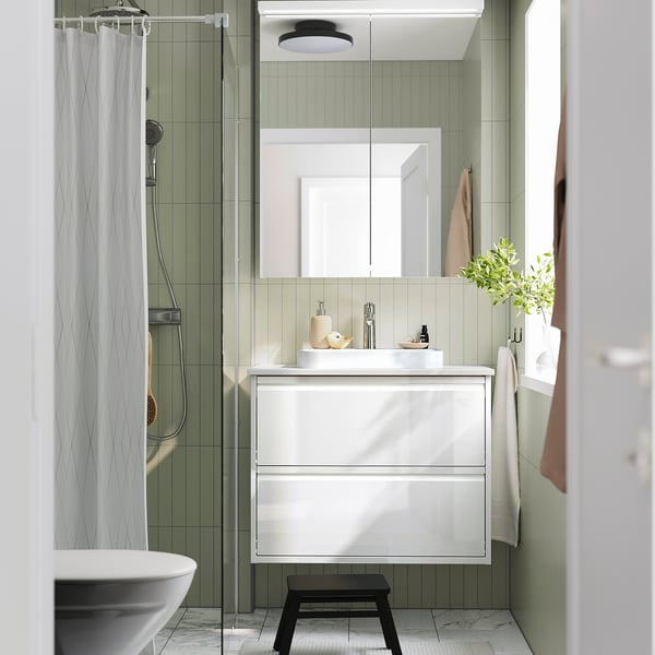 Tocador blanc modern amb lavabo, armari de miralls, tamboret i cortina de dutxa a ratlles.