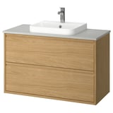 Tocador de bany modern de fusta clara amb lavabo blanc, tiradors mínims, dos calaixos i disseny de paret.