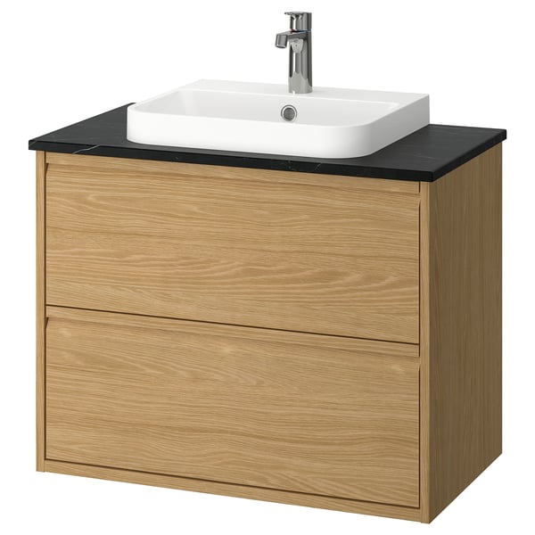 Tocador de bany modern de roure amb taulell negre i lavabo blanc. De paret amb disseny minimalista de calaixos.