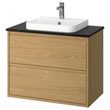 Tocador de bany modern de roure amb taulell negre i lavabo blanc. De paret amb disseny minimalista de calaixos.
