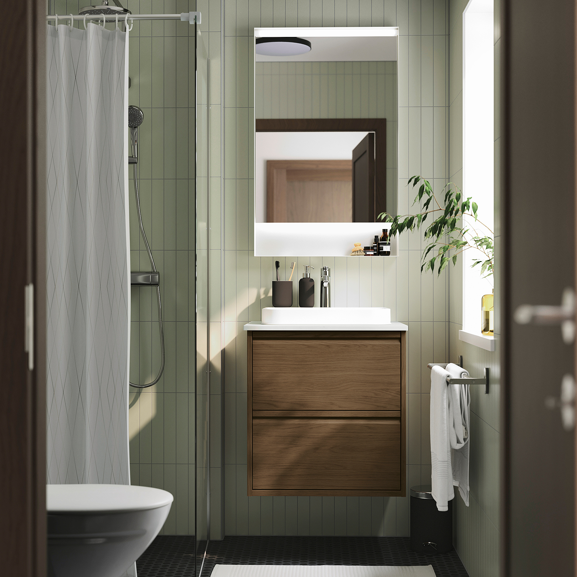 Bany modern amb rajoles verdes, armari de fusta, lavabo blanc, mirall, cortina de dutxa.