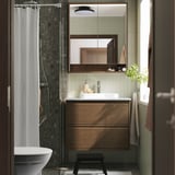Bany modern amb tocador de roure marró, lavabo de marbre, gran mirall i cortina de dutxa. Tamboret negre al davant.