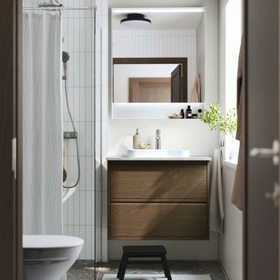 Bany modern: lavabo de fusta marró, taulell blanc, mirall; elegant, minimalista.