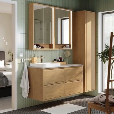 Bany modern amb armari de fusta clara, lavabo blanc i tovallola sota el mirall.