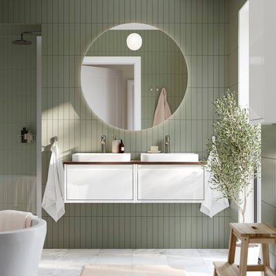 Bany modern de rajoles verdes amb gran mirall rodó, lavabo de marbre blanc i tamboret de fusta.