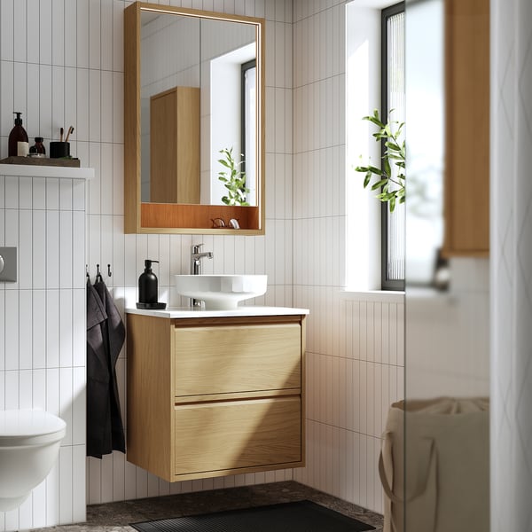 Bany modern amb tocador de roure ÄNGSJÖN, mirall, lavabo i accessoris minimalistes. De paret amb emmagatzematge.
