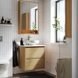 Bany modern amb tocador de roure ÄNGSJÖN, mirall, lavabo i accessoris minimalistes. De paret amb emmagatzematge.