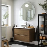 Bany modern minimalista: tocador de noguera, lavabo blanc, parets enrajolades, prestatges foscos, tovalloles, planta.