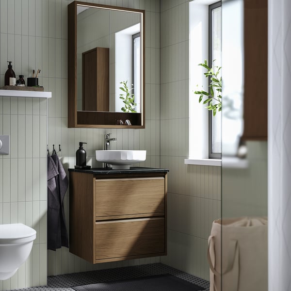 Bany modern amb tocador de noguera, lavabo, mirall, rajoles verdes, finestra de plantes.