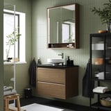 Configuració moderna del bany: moble ÄNGSJÖN en roure marró, lavabo central rodó, mirall, plantes, tovalloles, estil minimalista.