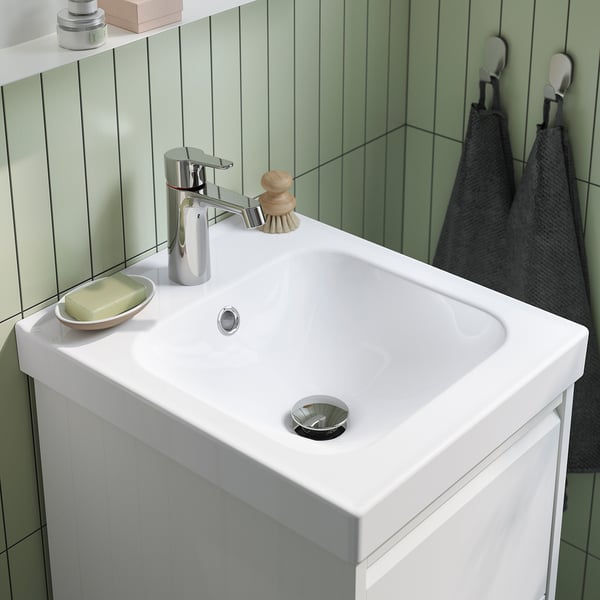Un lavabo de bany elegant i modern amb aixeta cromada, desguàs a joc, sabonera i ganxos de tovallola en una paret verda.