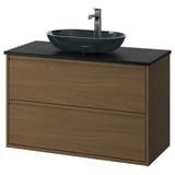 Tocador de bany modern amb fusta de noguera, taulell negre i lavabo de vidre.