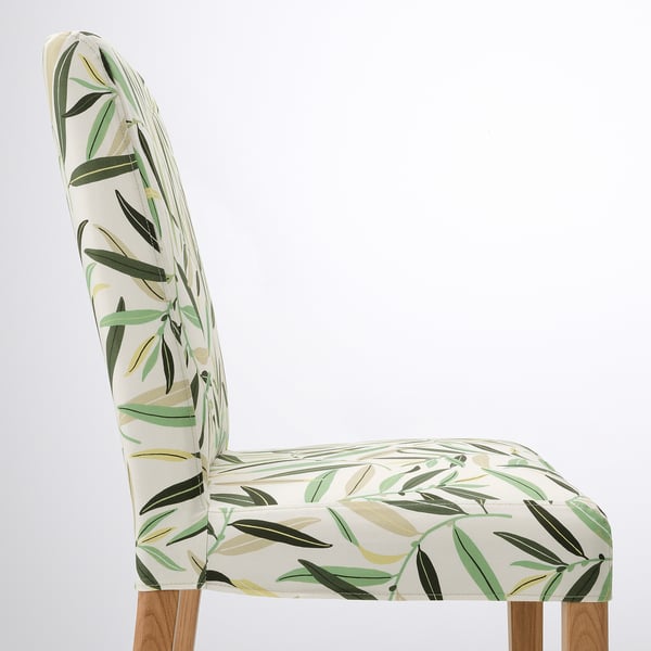 Cadira elegant amb respatller alt amb estampat de fulles verdes, respatller corbat, seient encoixinat i potes de fusta. Disseny modern, teixit ecològic.