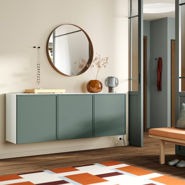 Aparador modern d'entrada BESTÅ en color verd amb tapa blanca brillant. Mirall rodó a sobre, gerro decoratiu i llums afegeixen estil. Banc de fusta a prop.