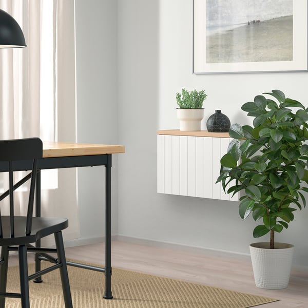 Habitació moderna amb prestatgeria BESTÅ, planta, gerro, cadira, taula i quadre gran. Decoració minimalista amb parets clares i catifa de jute.