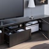 Suport de TV de fusta fosca amb calaixos oberts, que mostra l'emmagatzematge organitzat amb una làmpada a la part superior i un televisor de pantalla plana a sobre.