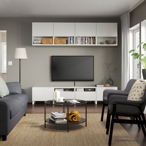 Sala d'estar moderna amb unitat de televisió BESTÅ, sofà gris, butaca, TV de pantalla plana, taula de cafè i planta.