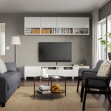 Sala d'estar moderna amb unitat de televisió BESTÅ, sofà gris, butaca, TV de pantalla plana, taula de cafè i planta.