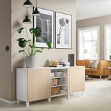 Sala d'estar moderna amb aparador BESTÅ blanc i fusta clara, planta d'interior, llums penjants, art emmarcat i sofà taronja.