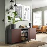 Sala d'estar moderna amb moble d'emmagatzematge BESTÅ granat, amb llibres, planta verda, llums penjants negres, sofà taronja, catifa natural i art de paret emmarcat.