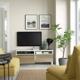 Sala d'estar moderna amb cadires grogues, TV de pantalla plana sobre suport BESTÅ blanc, amb calaixos per a l'emmagatzematge i la gestió de cables.