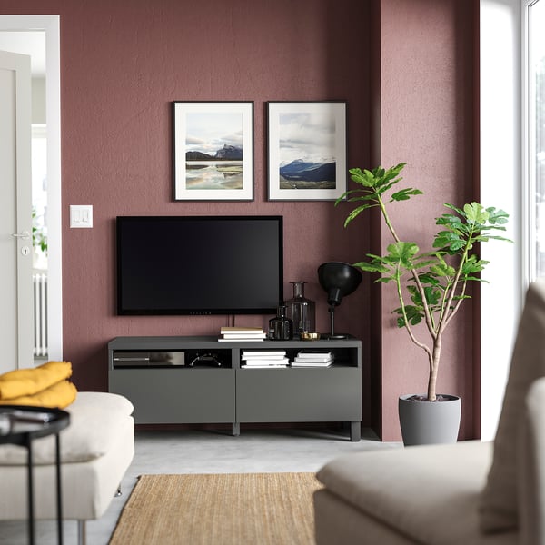 Sala d'estar moderna amb parets morades, sofà blanc, banc de TV BESTÅ gris, TV de pantalla plana, planta i quadres emmarcats.