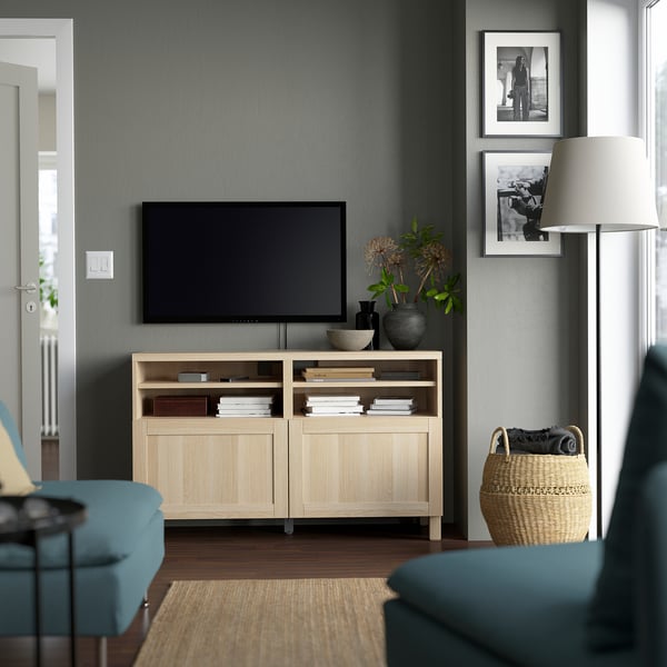 Sala d'estar moderna amb banc de TV BESTÅ de fusta clara, tv de pantalla plana, prestatgeries, llum, fotos i cistella.